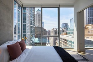 Una habitación de hotel moderna con una cama grande, vistas a la ciudad a través de ventanales del suelo al techo y un balcón.