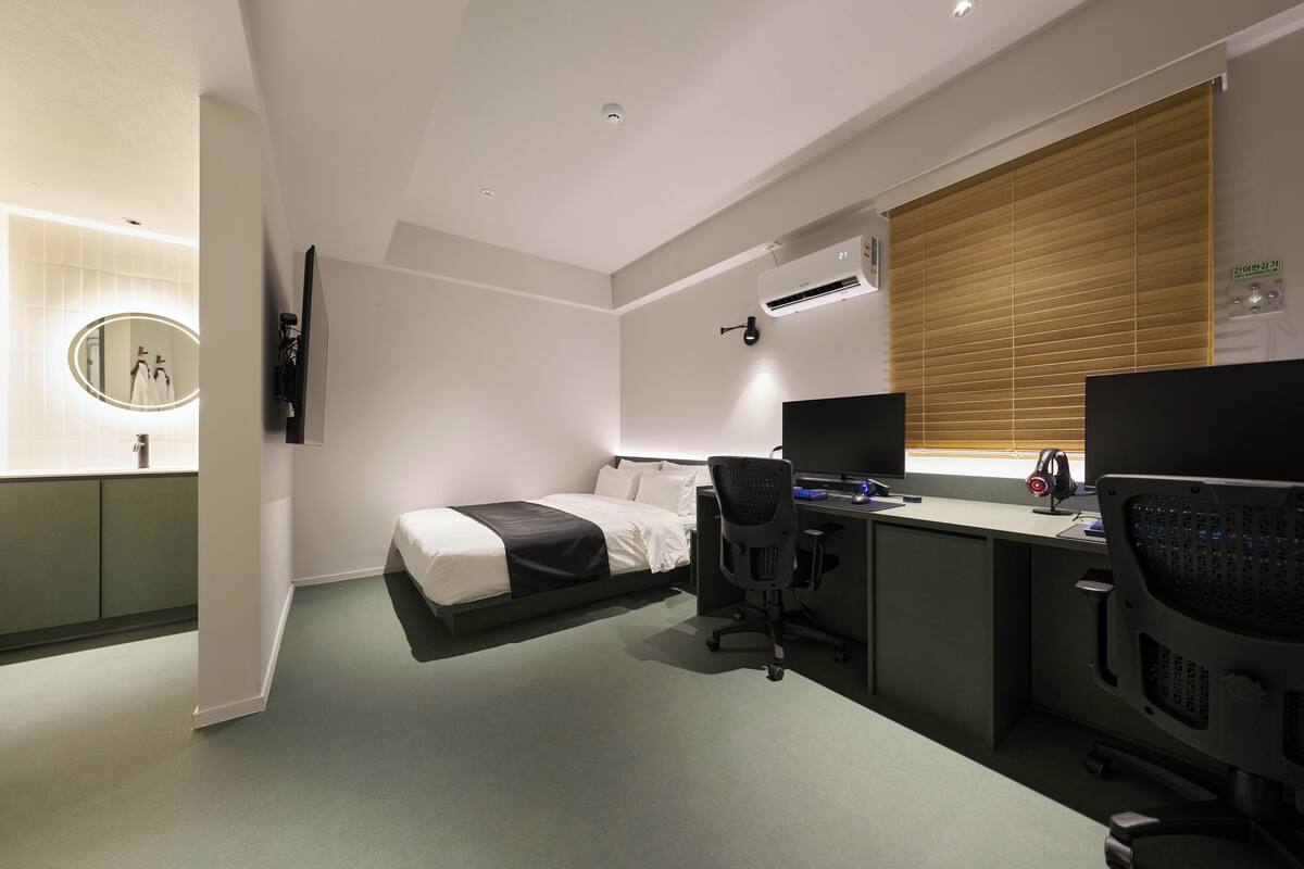 Una habitación de hotel con cama, escritorio, computadora y aire acondicionado.