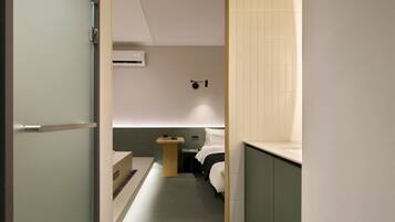 Un pasillo estrecho que conduce a un dormitorio con cama, mesita de noche y aire acondicionado instalado en la pared.