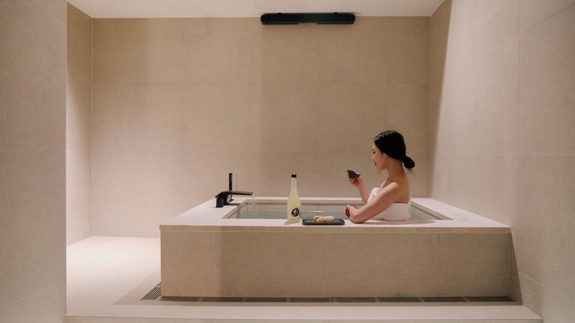 Une salle de bain moderne avec une baignoire, une bouteille et une serviette.