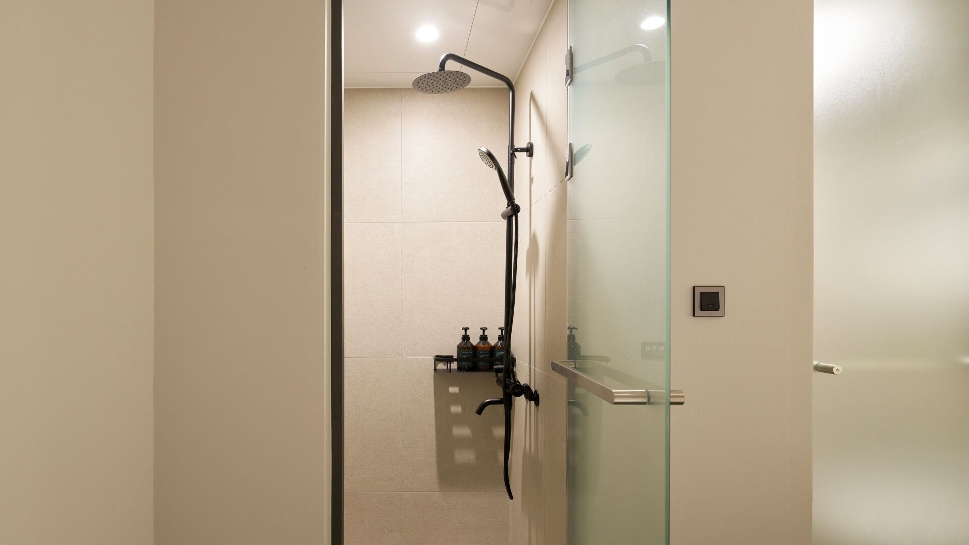 A modern bathroom with a glass shower enclosure, a handheld showerhead, and a wall-mounted faucet.