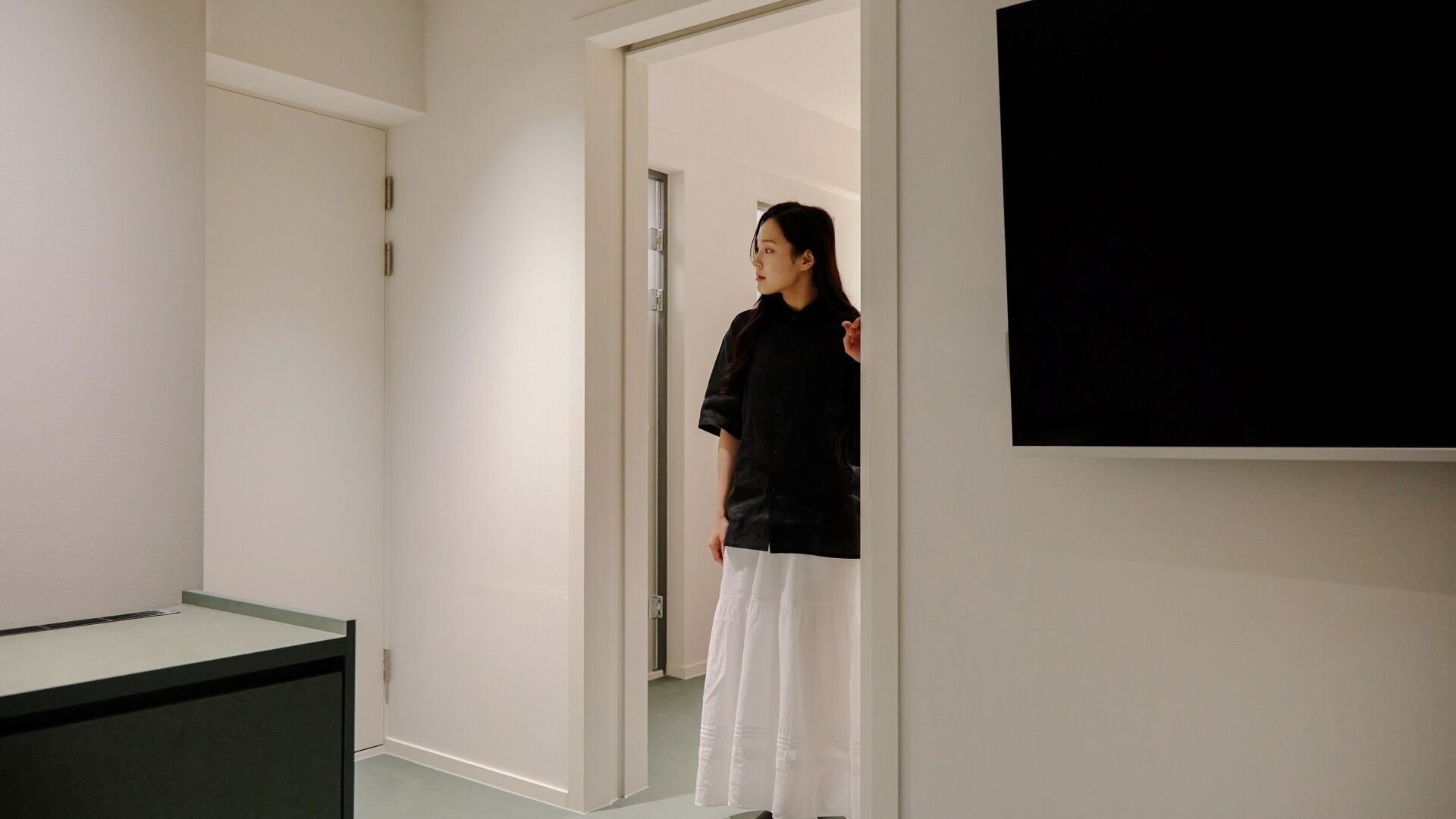 A person standing in a hallway with a door leading to another room.