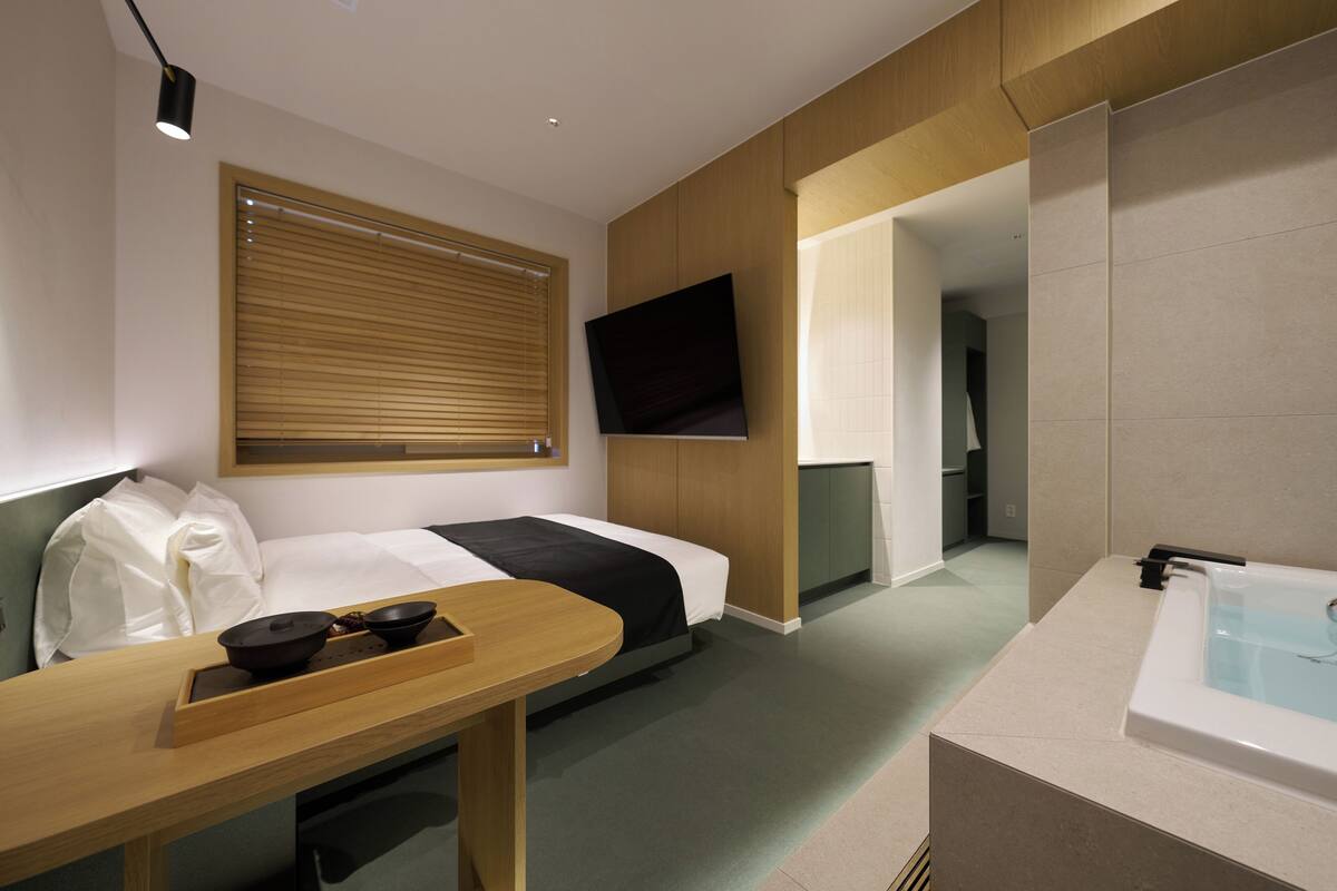 Habitación de hotel con cama, televisor montado en la pared, escritorio con bandeja y bañera.