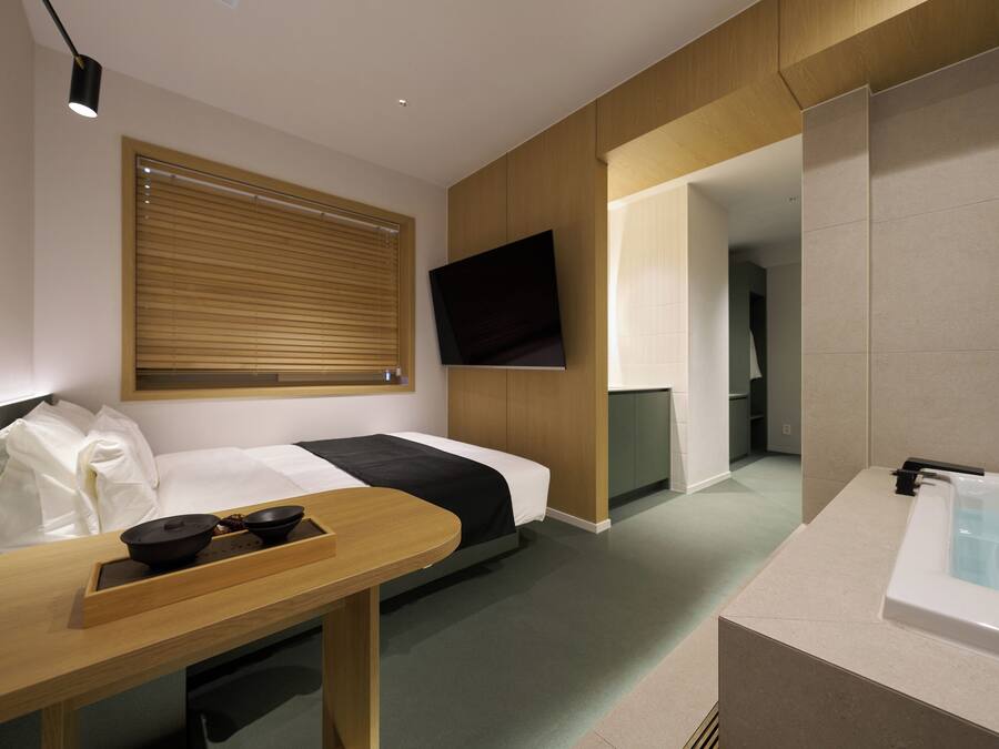 A hotel room with a bed, a TV mounted on the wall, a desk with a tray, and a bathtub.