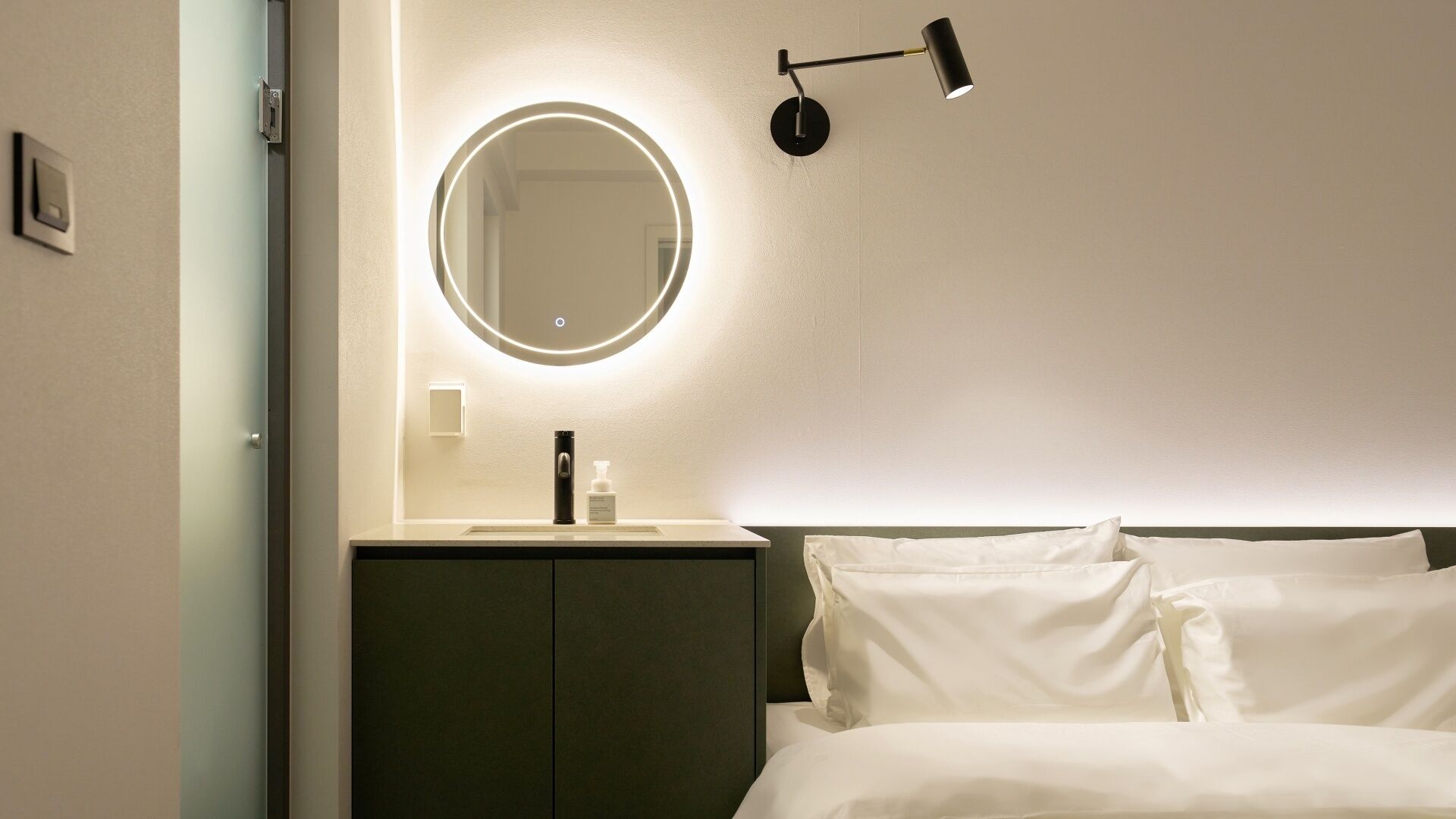A hotel room with a bed, a bedside table with a lamp, a mirror, and a small cabinet.