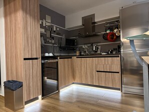 Eine moderne Küche mit Holzschränken, einem Einbauofen, einem Edelstahlkühlschrank und einer Mikrowelle.