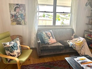 Ein Wohnzimmer mit einem grünen Sessel, einer Couch und einem Fenster mit Blick auf einen Zaun und Grünflächen.