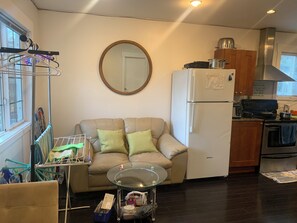 Ein kompakter Wohnbereich mit Sofa, Glastisch, Küchenzeile inklusive Kühlschrank und Herd sowie einer Wäscheständer.