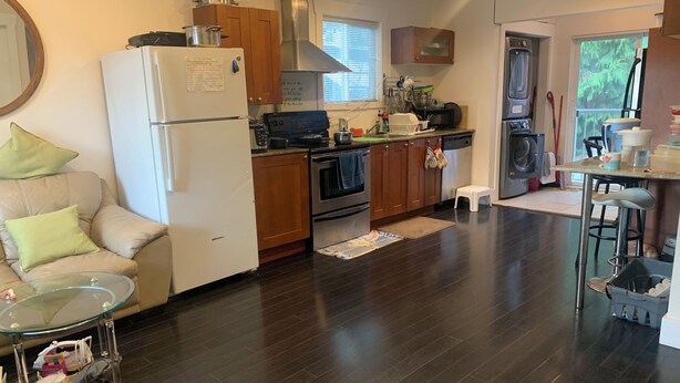 A modern kitchen with a refrigerator, stove, and oven. There is a dining area with a glass table and a sofa. - Gorgeous 4-bedroom house in Vancouver perfect for your getaway (Vancouver)