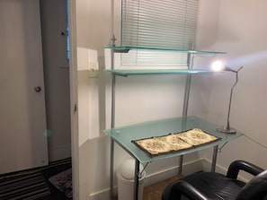 Ein Zimmer mit einem Glastisch, einem Stuhl, einer Lampe und einem Fenster mit Jalousien.