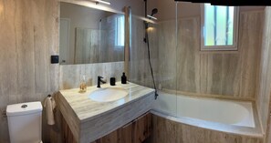 Een badkamer met een marmeren wastafel, een grote spiegel, een toilet en een bad.