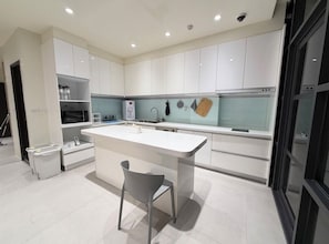 A modern kitchen with white cabinetry, a central island, and a grey chair. - Phoenix Landing (Tainan)