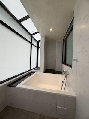 A modern bathroom with a large bathtub, skylight, and marble tiles. - Phoenix Landing (Tainan)