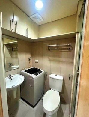 A compact bathroom with a sink, toilet, and built-in washing machine. - MOA Staycation - MOA Homestay (Pasay City)