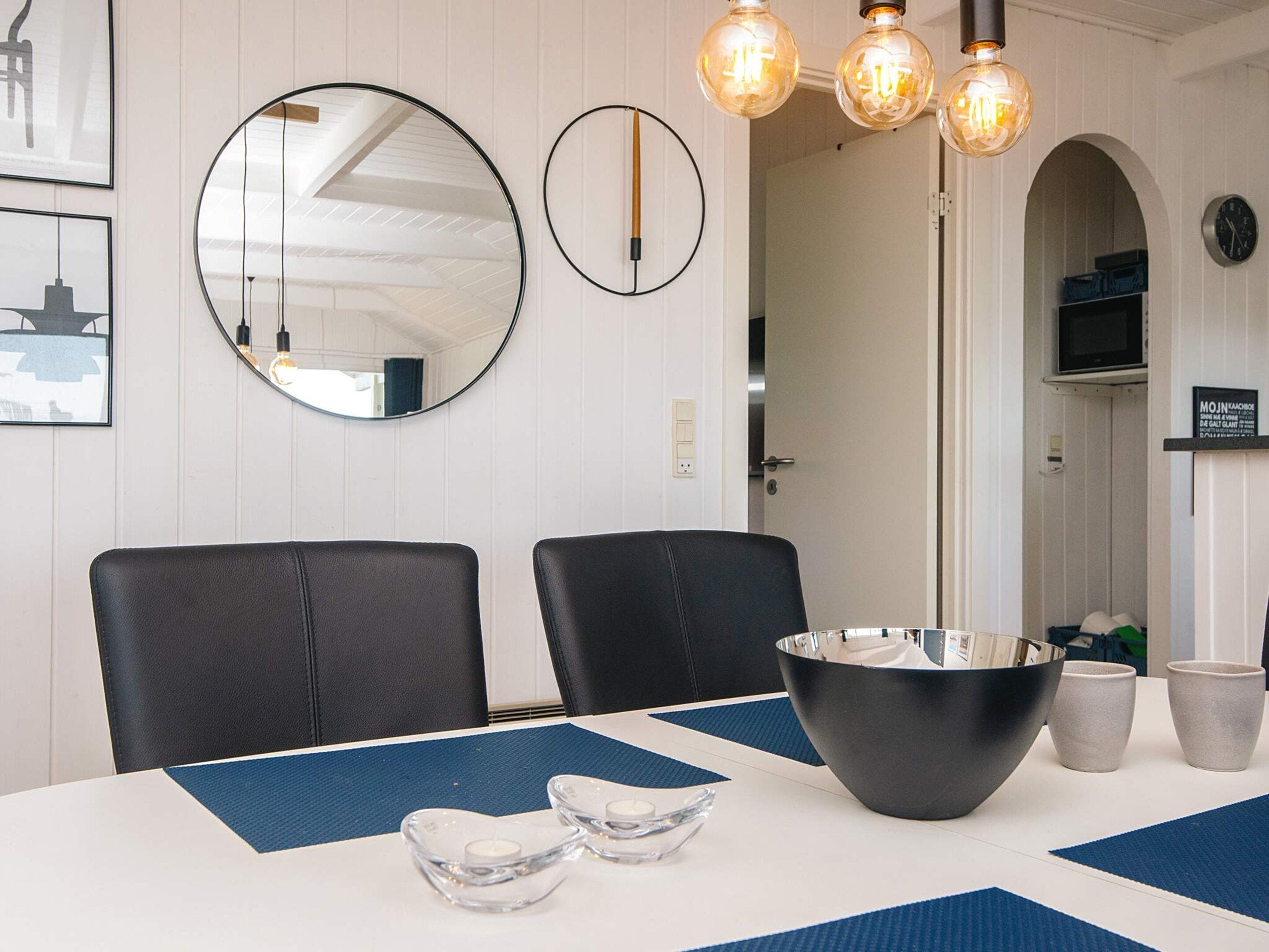 A dining area with a white table, two black chairs, a large black bowl, two clear candle holders, and a blue placemat.