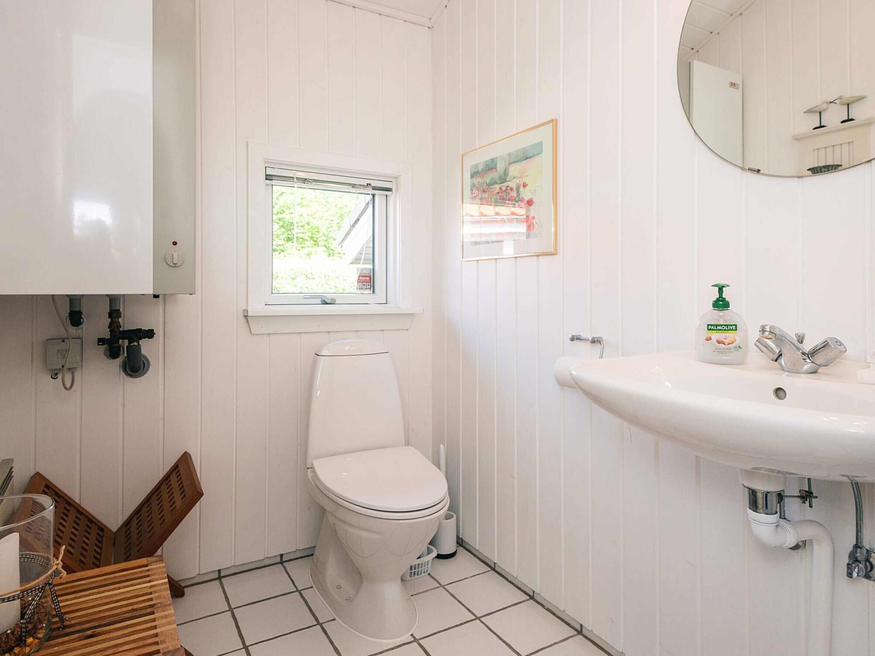 Een kleine, schone badkamer met toilet, wastafel, raam en spiegel.