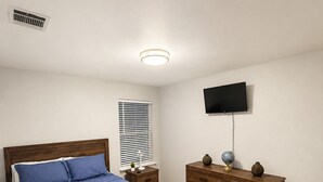 Quarto com cama, penteadeira, televisão e janela com persianas.