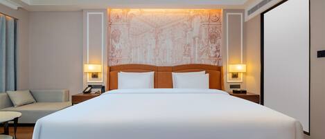Una habitación de hotel con una cama grande, dos mesitas de noche con lámparas, un sofá y una alfombra estampada.