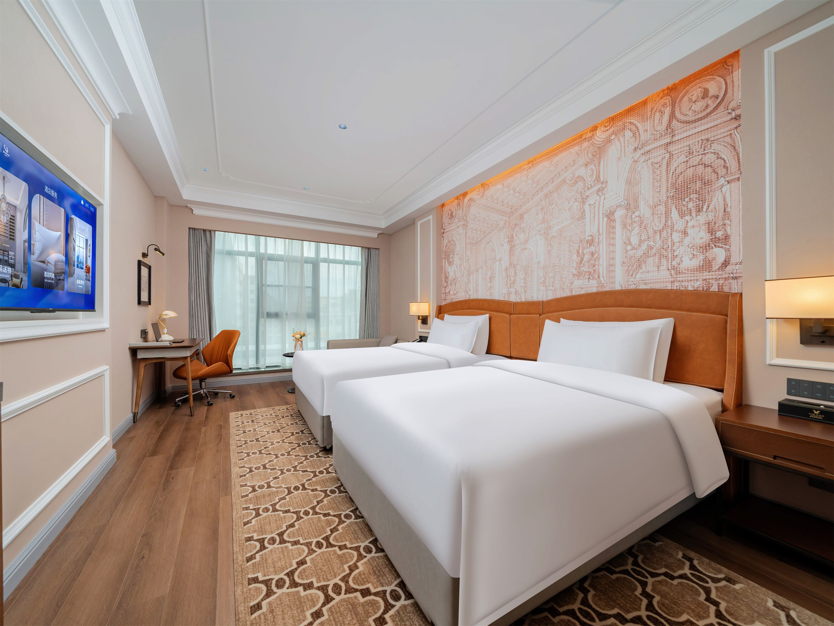 Quarto de hotel com duas camas, uma escrivaninha, uma cadeira, uma televisão e uma janela grande.
