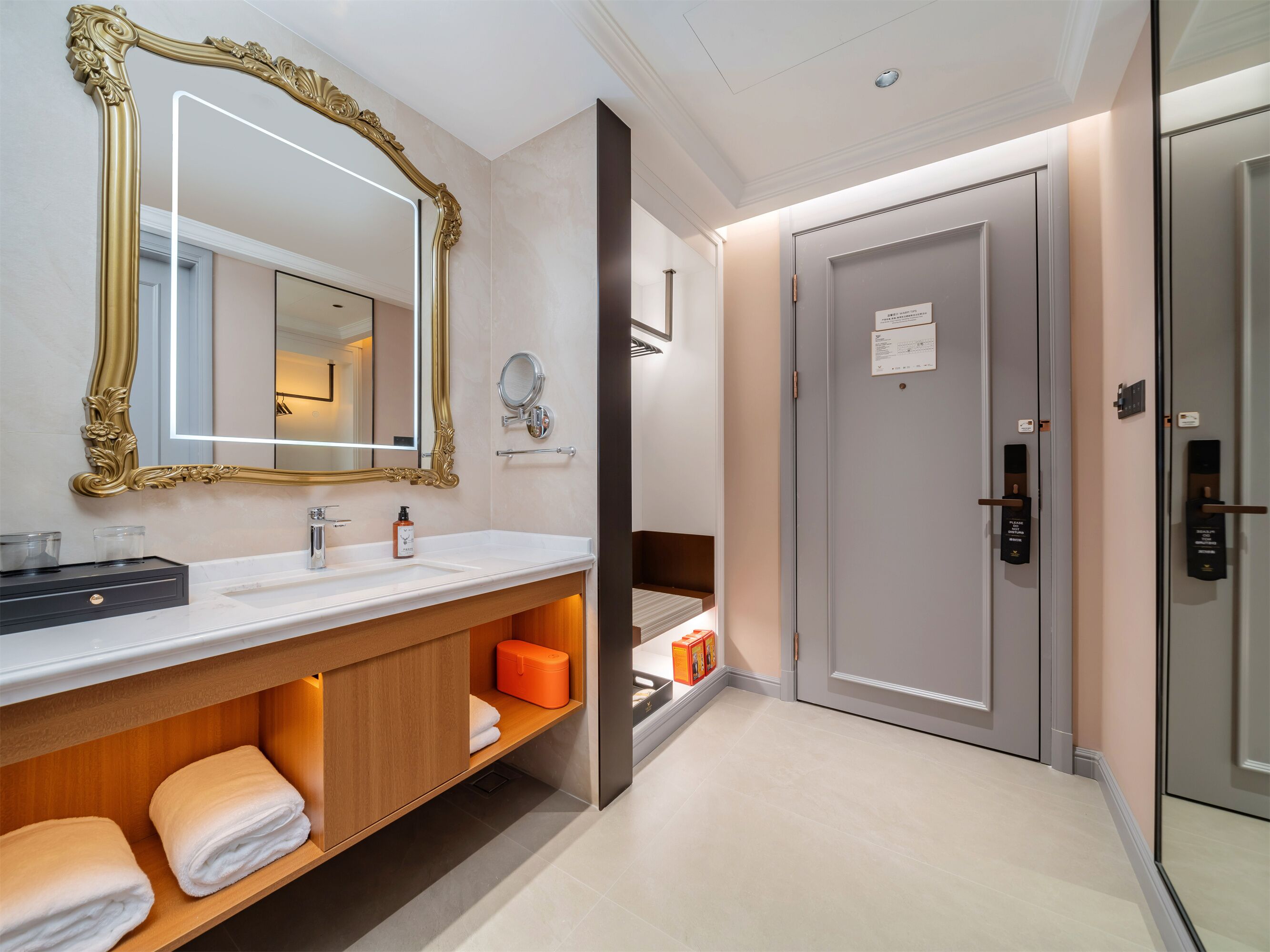 A hotel bathroom with a large ornate mirror, a sink, a towel rack, and a door with a keycard lock.