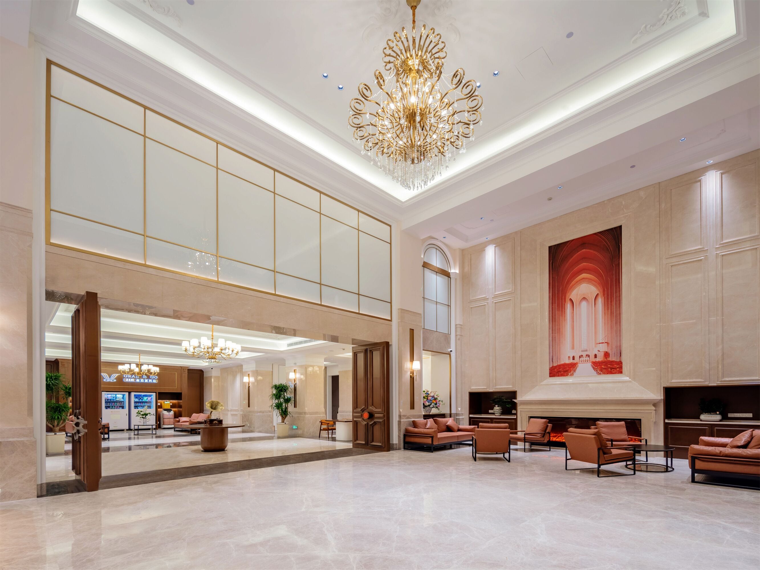 A spacious lobby with a high ceiling, a grand chandelier, seating areas, and a large wall mural.
