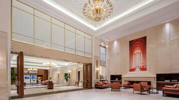 A spacious lobby with a high ceiling, a grand chandelier, seating areas, and a large wall mural.