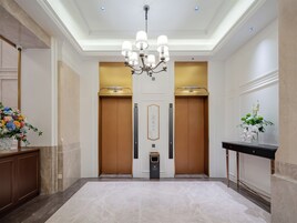 Una hall d'albergo con un lampadario, due ascensori, una reception e un pavimento in marmo.