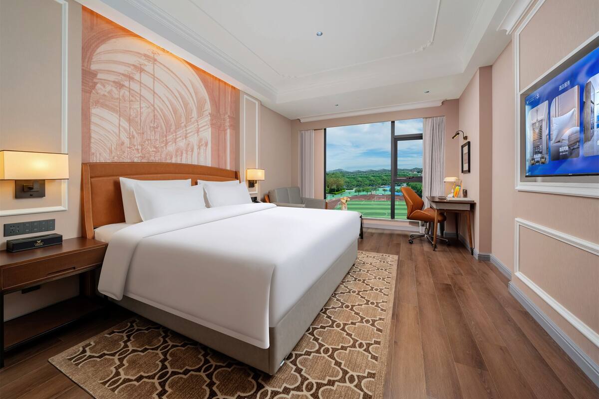 Ein Hotelzimmer mit einem großen Bett, einem Schreibtisch mit Stuhl, einem Fernseher und Blick auf einen Golfplatz.