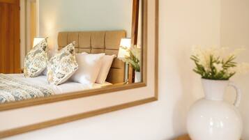 A bedroom with a bed, pillows, a bedside lamp, and a vase with flowers.