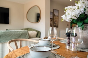 Une table à manger dressée avec des assiettes, des bols et des verres à vin, et un vase de fleurs en arrière-plan.