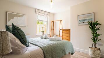 A bedroom with a bed, pillows, a green blanket, a window with a view, a ladder, a plant, and artwork on the walls.