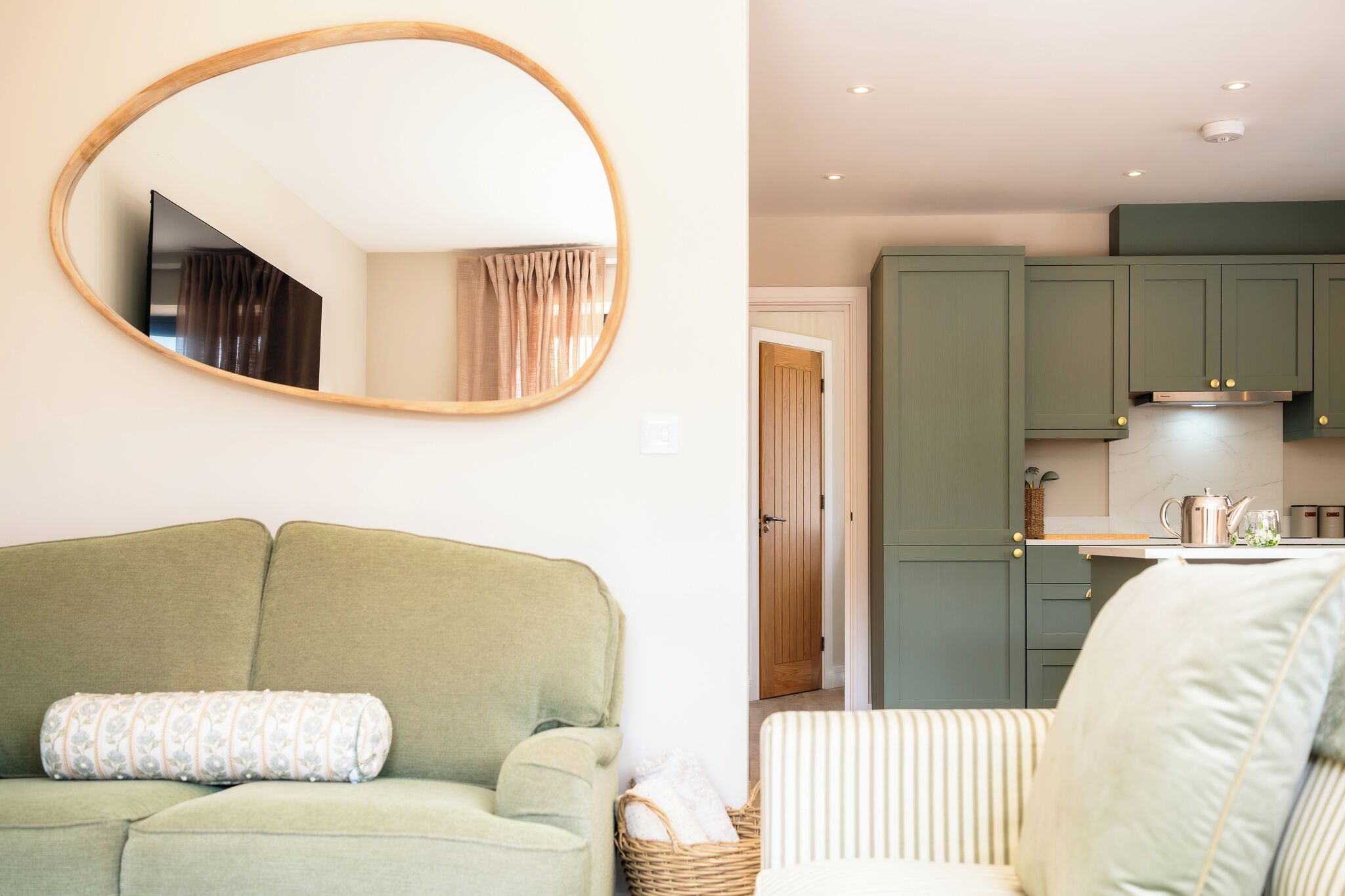 A living room with a green sofa, a round mirror, and a striped chair.
