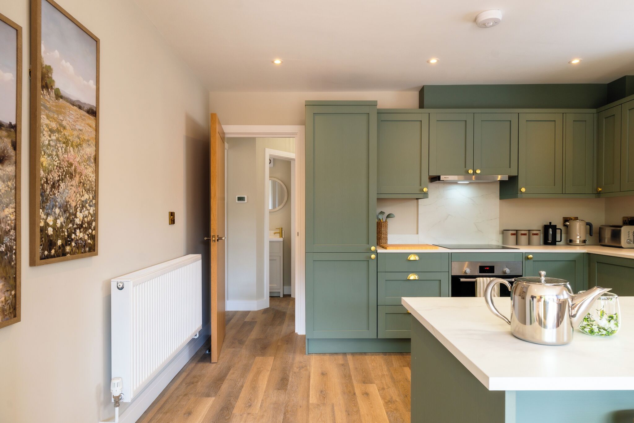 A kitchen with green cabinets, a white countertop, and a kettle.
