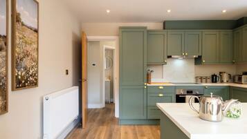 A kitchen with green cabinets, a white countertop, and a kettle.