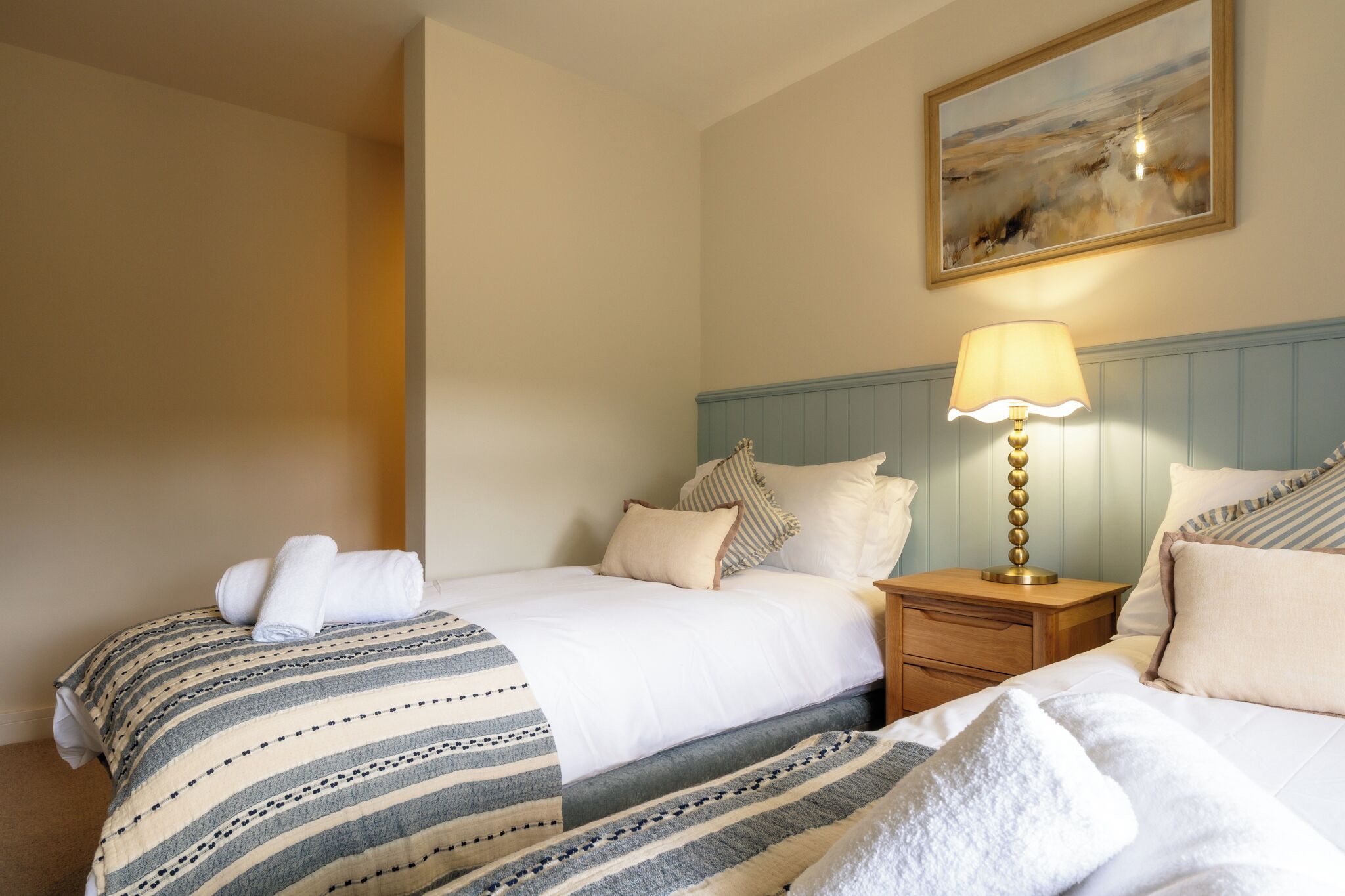 Habitación de hotel con dos camas, una mesita de noche con lámpara y un cuadro en la pared.
