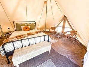Uma tenda com uma cama, um banco, uma cadeira e uma pequena mesa.