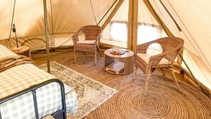 Una carpa con una cama, dos sillas de mimbre, una mesita y una alfombra tejida.