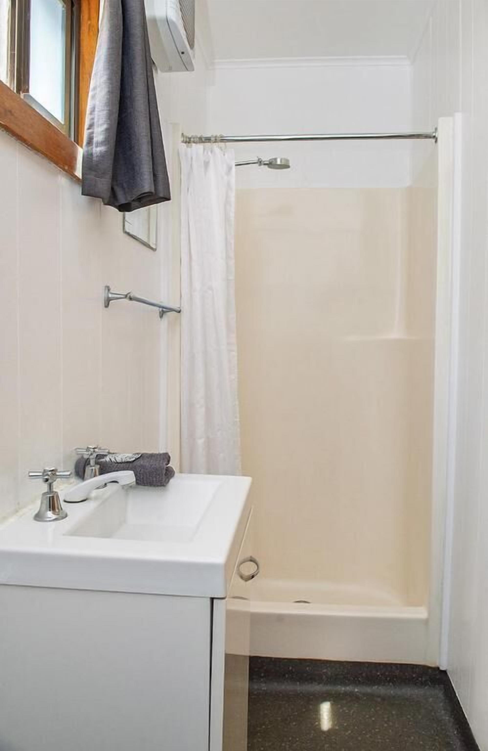 Un baño con un lavamanos blanco, una ducha con cortina y una toalla colgada en la pared.