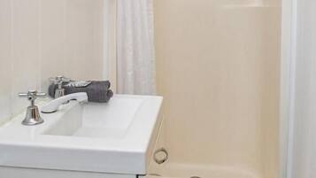 Un baño con un lavamanos blanco, una ducha con cortina y una toalla colgada en la pared.