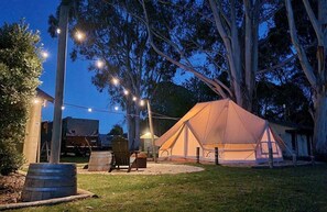 A tent set up in a grassy area with trees, a wooden chair, and a barrel.