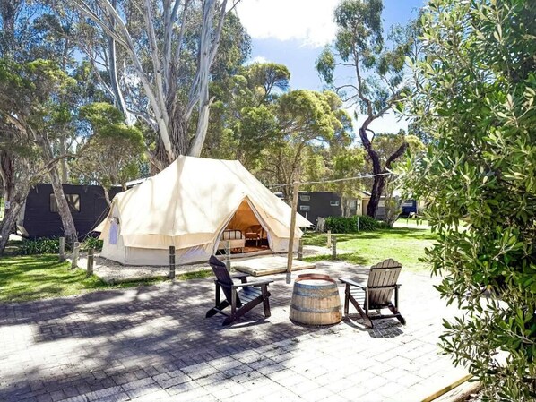Alojamiento en carpa con zona de patio, asientos al aire libre y árboles circundantes.