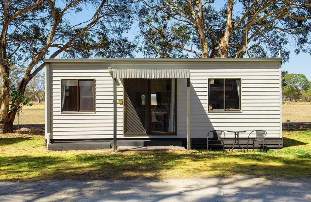 A small, single-story mobile home with a covered porch, two windows, and a door.