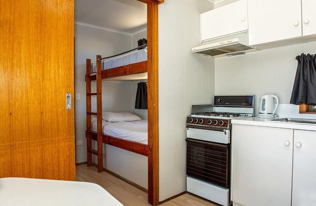 Una habitación compacta con literas, una kitchenette equipada con estufa y tetera, y una puerta de madera.