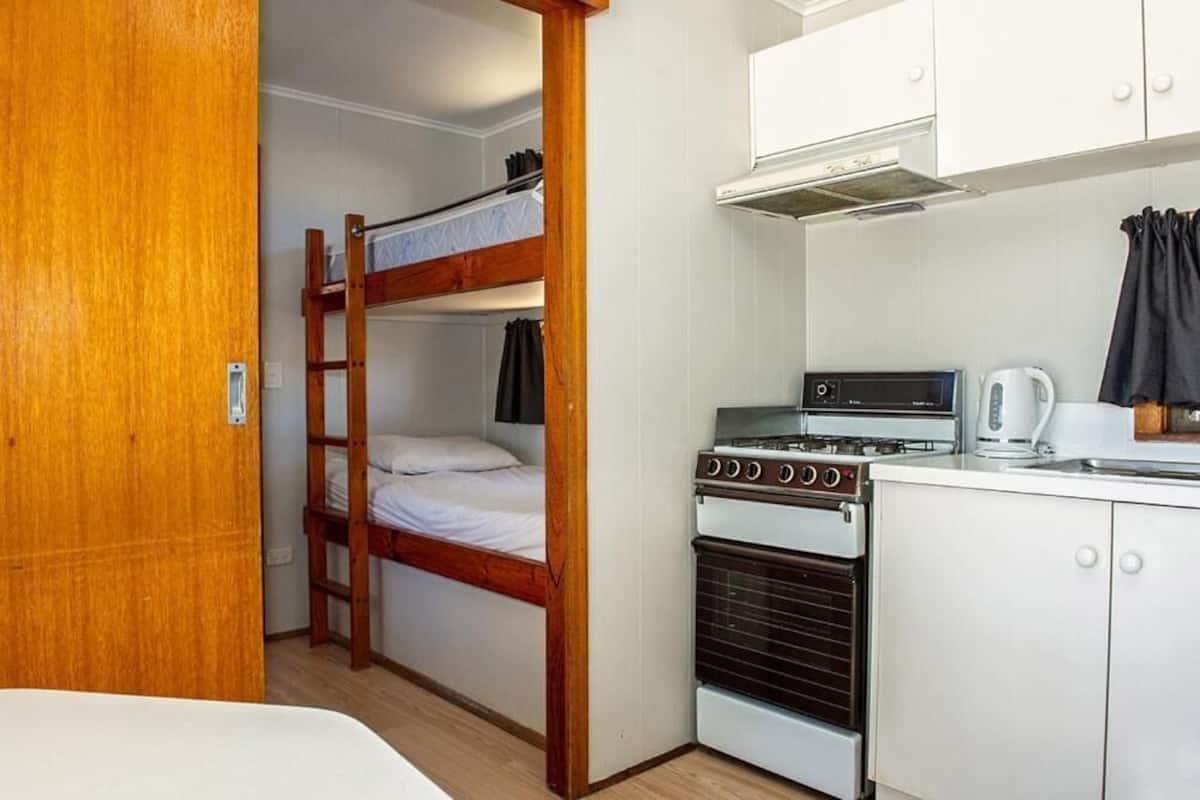 A compact room with bunk beds, a kitchenette with a stove and kettle, and a wooden door.
