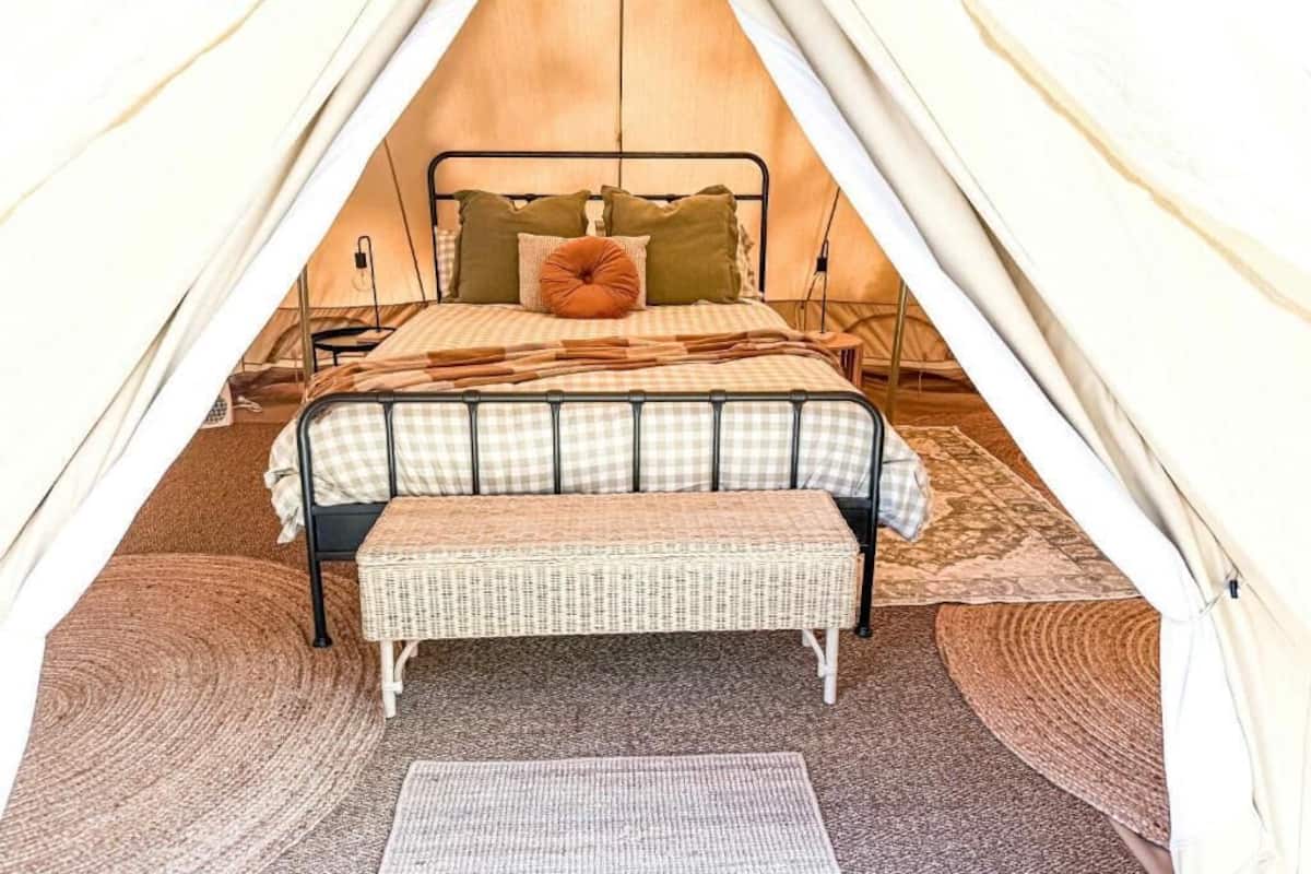 Une tente équipée d’un lit, d’oreillers, d’un banc et d’un tapis.