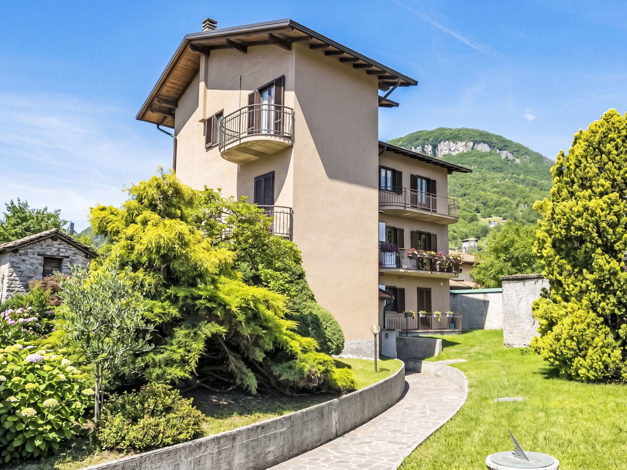 A multi-story building with balconies, surrounded by lush greenery and a mountainous backdrop.