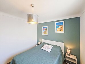 A bedroom with a bed, two wall-mounted lamps, a hanging light fixture, and two framed posters on the wall. - Croix du Sud by Interhome (Canet-Plage)