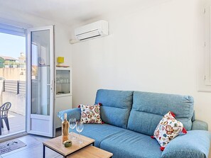 A living room with a blue sofa, a small table with a bottle and glasses, and a glass cabinet with shelves. - Croix du Sud by Interhome (Canet-Plage)