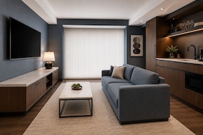 A modern living room with a sofa, coffee table, TV, and kitchen area. - The Quarry Hotel (Toronto)