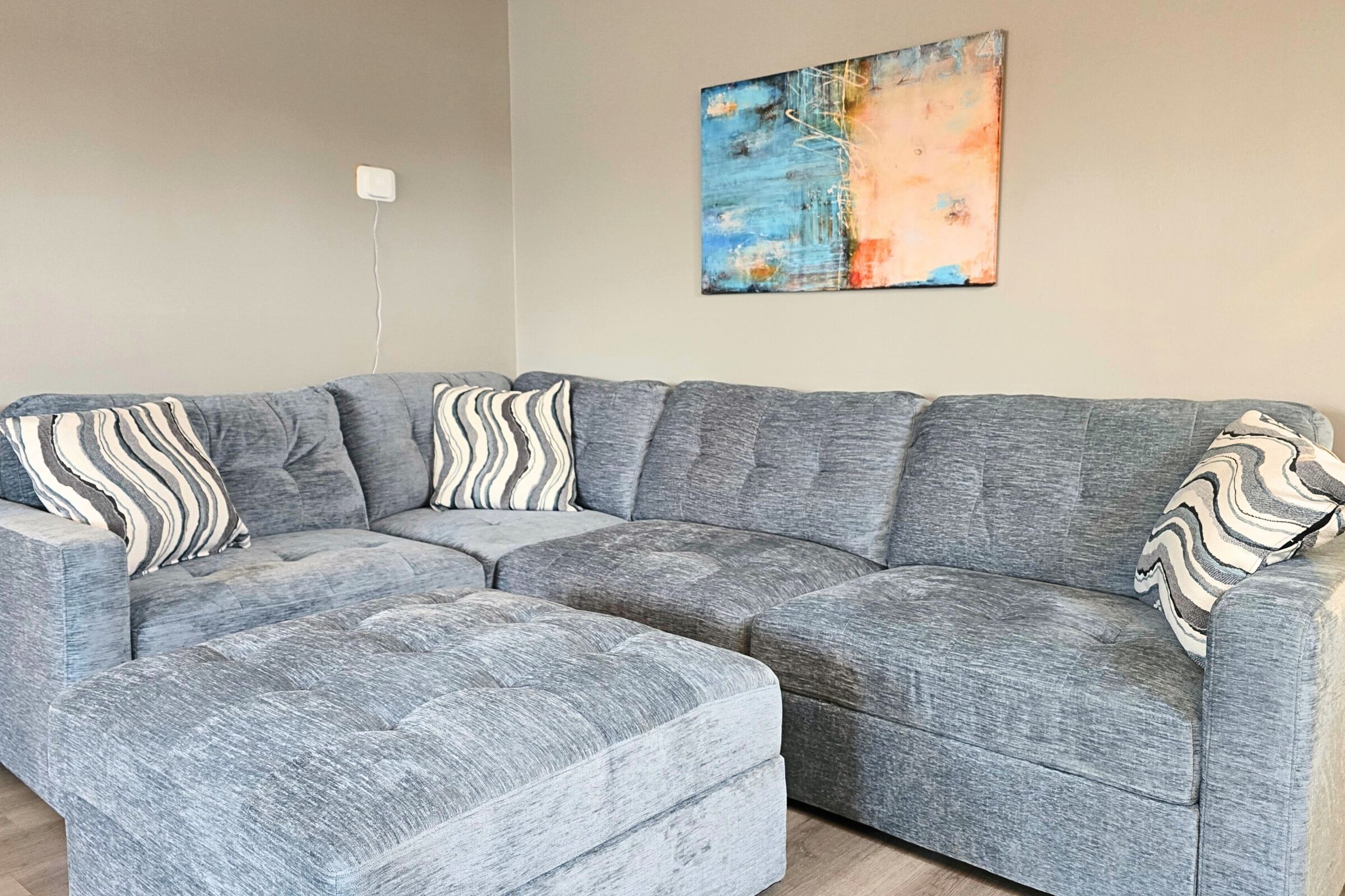 Plush sectional with ottoman, chic art, and comfy lounge-ready vibes.